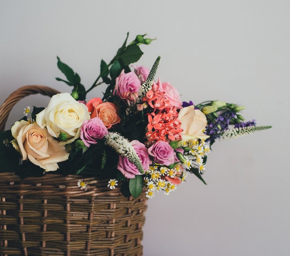 Zdjęcie przedstawiające bukiet kwiatów w wiklinowym koszu na szarym tle